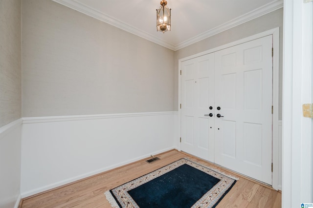 entryway with an inviting chandelier, wood finished floors, visible vents, and crown molding