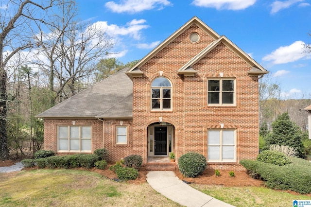 traditional-style home with roof with shingles, a front yard, and brick siding