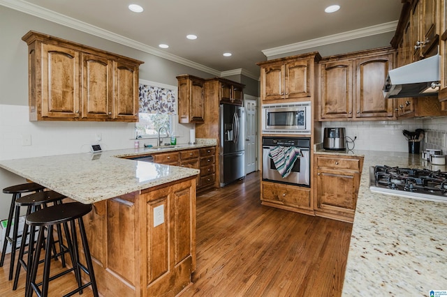 kitchen with under cabinet range hood, stainless steel appliances, a peninsula, light stone countertops, and dark wood-style floors