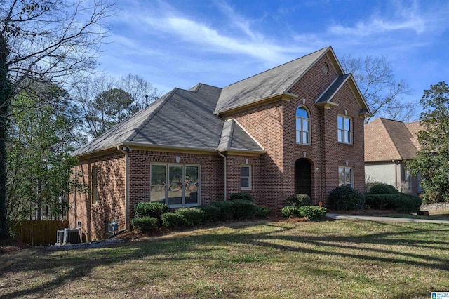 view of front of home with a shingled roof, a front yard, and brick siding