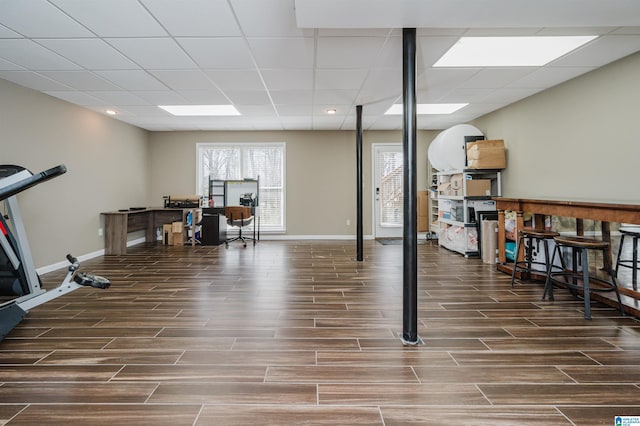 exercise area featuring wood finish floors, a paneled ceiling, and baseboards