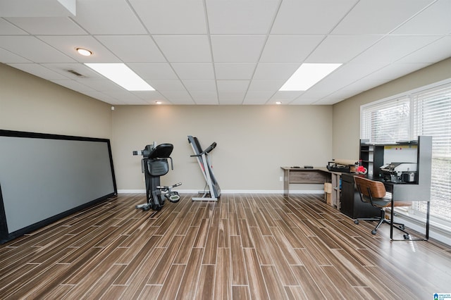 interior space with visible vents, a drop ceiling, baseboards, and wood finished floors