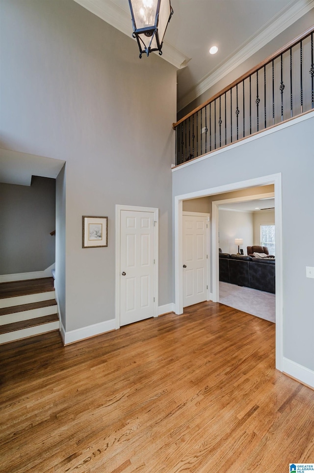 unfurnished living room featuring baseboards, crown molding, a high ceiling, and wood finished floors