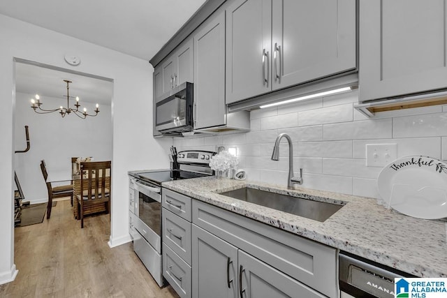 kitchen featuring stainless steel appliances, a sink, gray cabinets, light stone countertops, and light wood finished floors