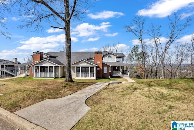 view of front of house with covered porch, brick siding, a chimney, and a front yard