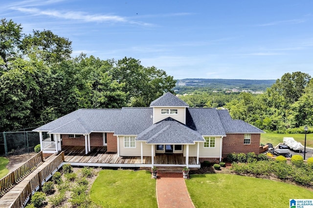 ranch-style house featuring brick siding, fence, roof with shingles, a wooden deck, and a front yard