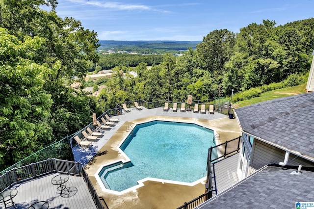 community pool with stairs, fence, a view of trees, and a patio