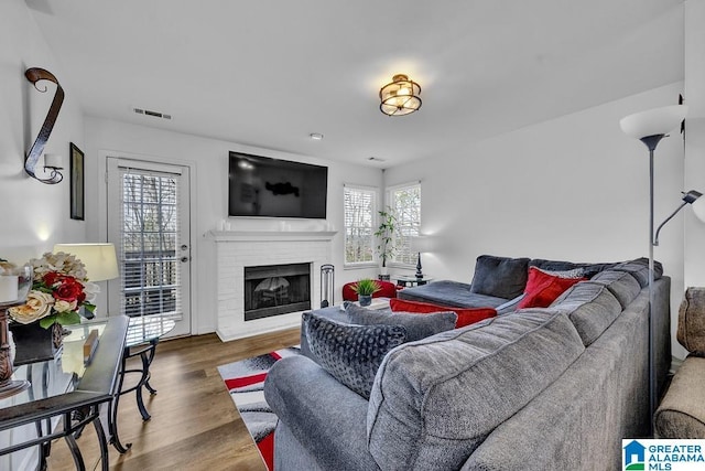 living area featuring a brick fireplace, wood finished floors, and visible vents