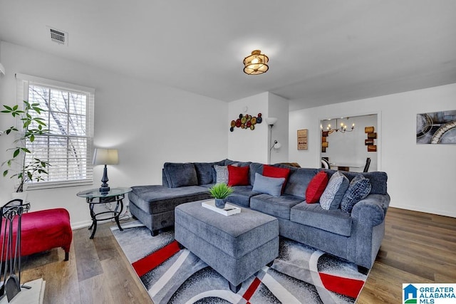 living room featuring an inviting chandelier, baseboards, visible vents, and wood finished floors