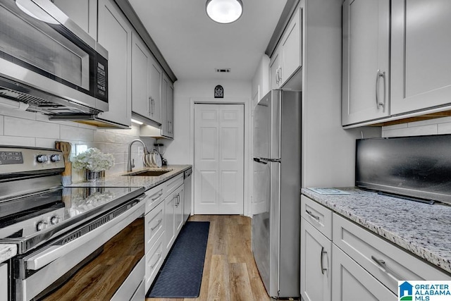 kitchen featuring backsplash, light stone countertops, stainless steel appliances, light wood-style floors, and a sink