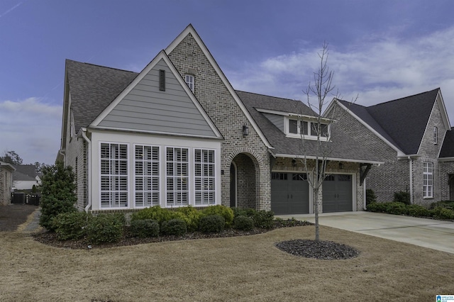 view of front facade with a garage, driveway, brick siding, and roof with shingles