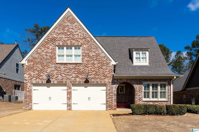 view of front of property with an attached garage, central air condition unit, brick siding, concrete driveway, and roof with shingles