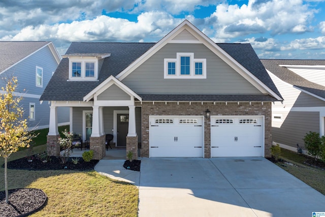 craftsman-style house with a shingled roof, covered porch, an attached garage, driveway, and a front lawn