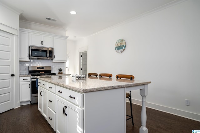 kitchen with visible vents, an island with sink, appliances with stainless steel finishes, a kitchen breakfast bar, and white cabinetry