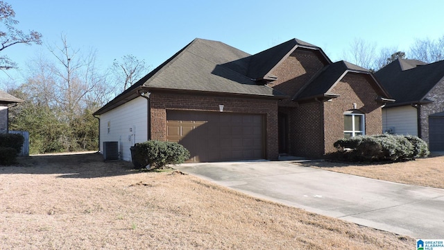 view of front of property with central AC unit, a garage, brick siding, a shingled roof, and concrete driveway