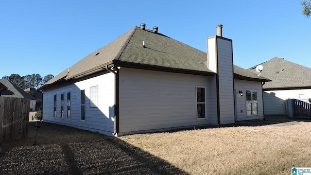 back of house featuring a chimney, fence, and roof with shingles