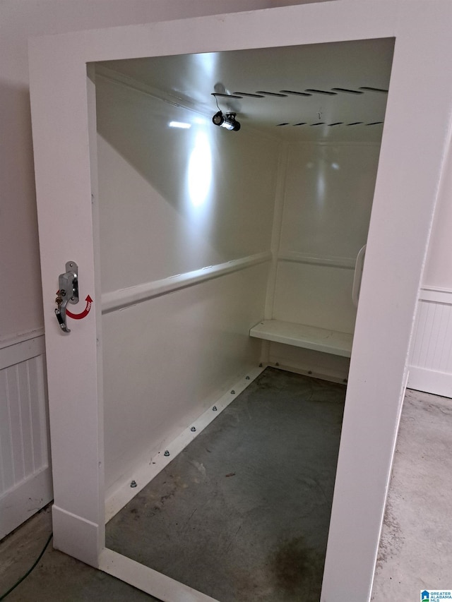 bathroom with concrete floors, wainscoting, elevator, and a decorative wall