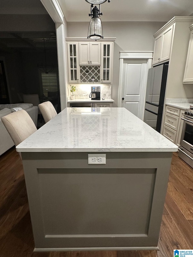 kitchen featuring decorative backsplash, a kitchen island, glass insert cabinets, appliances with stainless steel finishes, and light stone countertops