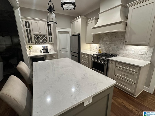 kitchen with dark wood-type flooring, premium range hood, high end stainless steel range oven, freestanding refrigerator, and glass insert cabinets