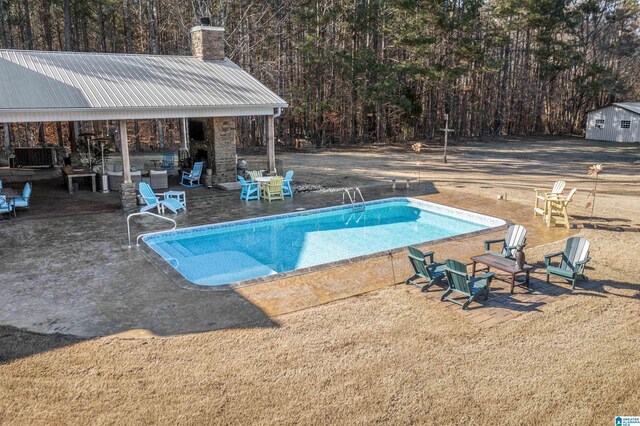 outdoor pool with a fireplace, an outbuilding, and a patio