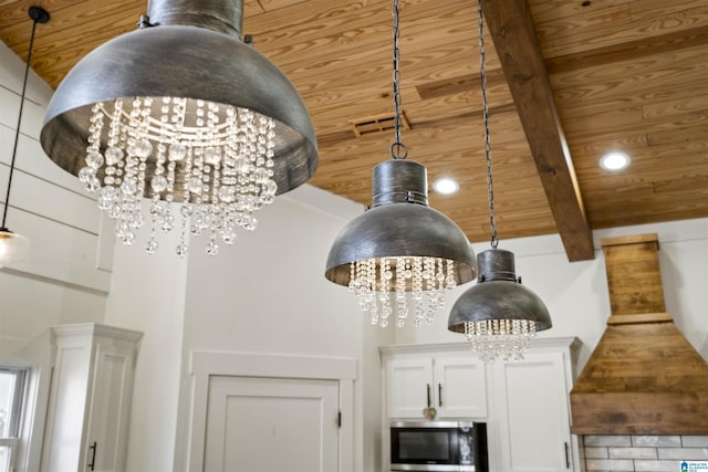 interior details with beam ceiling, stainless steel microwave, an inviting chandelier, wood ceiling, and white cabinets