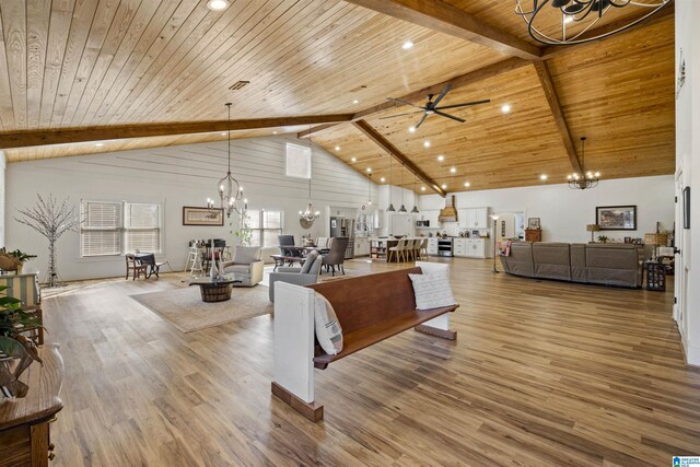living room with high vaulted ceiling, wooden ceiling, ceiling fan with notable chandelier, wood finished floors, and beam ceiling