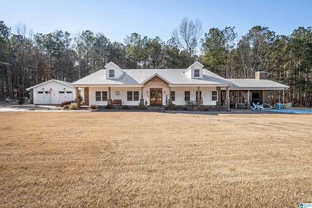 view of front of house with covered porch, metal roof, a front lawn, and a detached garage