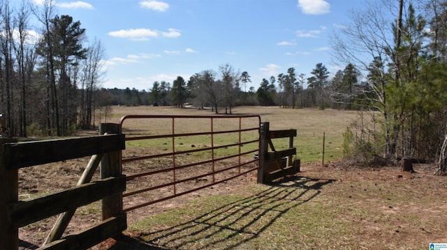 view of gate with a rural view, fence, and a lawn