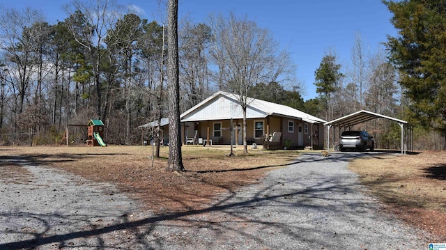 view of front of property featuring playground community, a carport, a porch, and gravel driveway