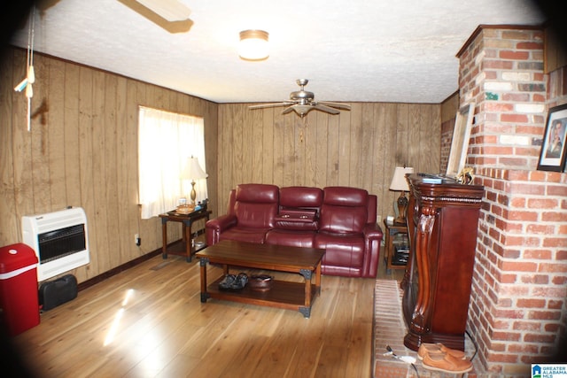 living room featuring wood walls, wood finished floors, a ceiling fan, baseboards, and heating unit