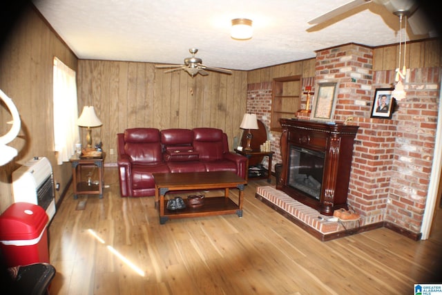 living area featuring heating unit, ceiling fan, wood finished floors, and a glass covered fireplace