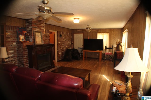 living room with wood walls, ceiling fan, a fireplace, and wood finished floors