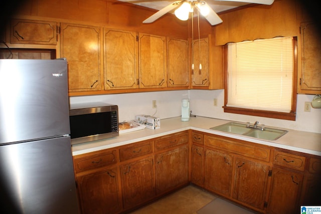 kitchen featuring stainless steel appliances, a sink, a ceiling fan, light countertops, and brown cabinetry