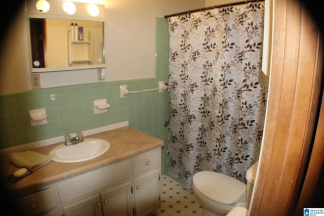 bathroom with a shower with shower curtain, wainscoting, toilet, vanity, and tile walls