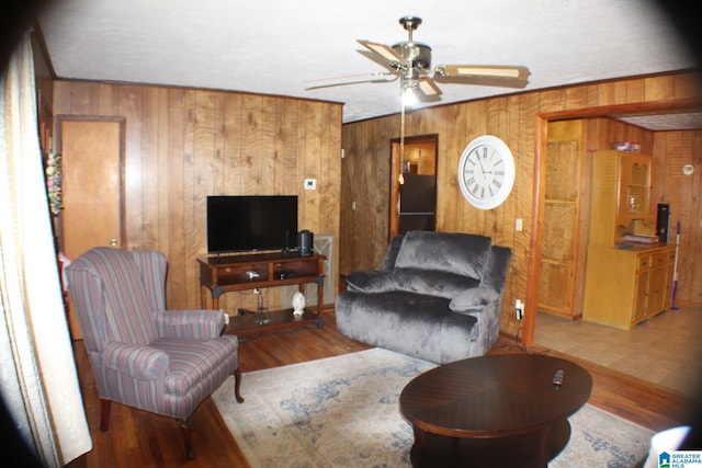 living room with wood walls, wood finished floors, and a ceiling fan