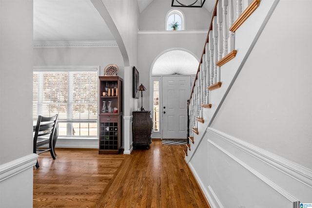 entryway featuring stairs, arched walkways, high vaulted ceiling, and wood finished floors