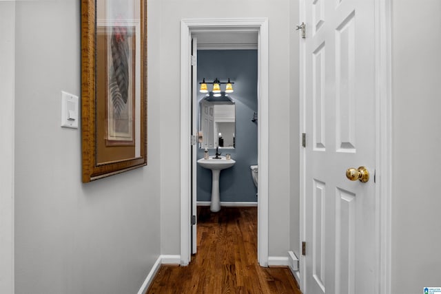 hallway with dark wood-style flooring, a sink, and baseboards