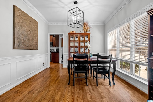 dining space featuring ornamental molding, a chandelier, a decorative wall, and wood finished floors