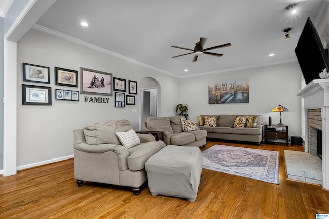 living area with arched walkways, ornamental molding, a brick fireplace, and wood finished floors