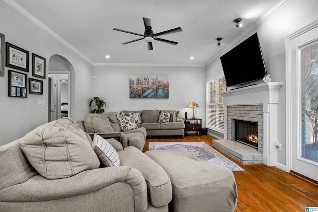 living area featuring arched walkways, a fireplace, wood finished floors, and a healthy amount of sunlight