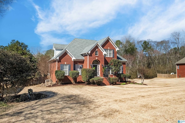 traditional-style home featuring brick siding, a front yard, and fence