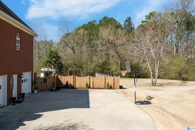 view of patio with a garage, driveway, a wooded view, and fence