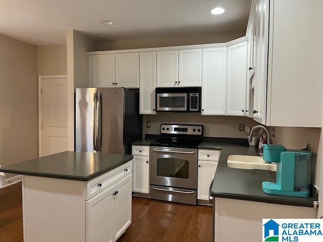 kitchen with appliances with stainless steel finishes, dark countertops, a sink, and a kitchen island