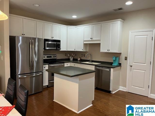 kitchen featuring a center island, dark countertops, appliances with stainless steel finishes, white cabinets, and a sink