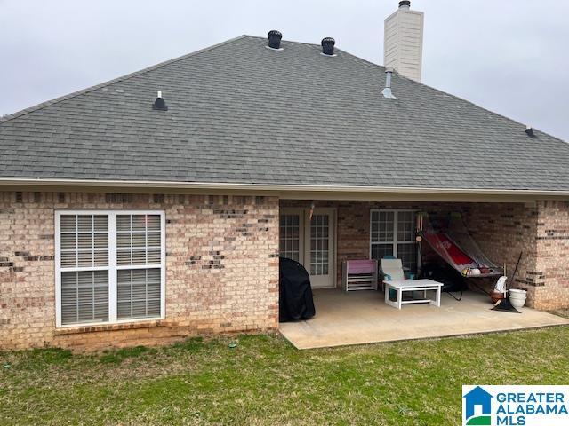 rear view of property featuring a patio area, roof with shingles, a lawn, and brick siding