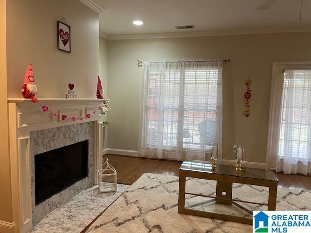 interior space featuring a premium fireplace, wood finished floors, visible vents, a healthy amount of sunlight, and crown molding