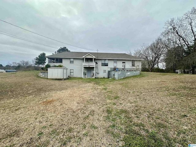 rear view of house featuring a yard, a balcony, an outdoor structure, and a storage unit