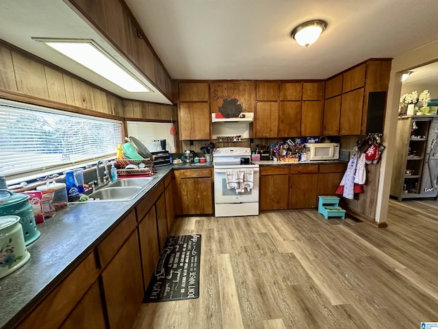 kitchen featuring light wood-style flooring, white appliances, a sink, brown cabinetry, and dark countertops