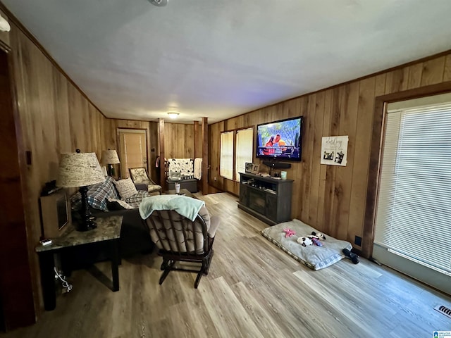 living area with a healthy amount of sunlight, light wood-style flooring, wooden walls, and crown molding