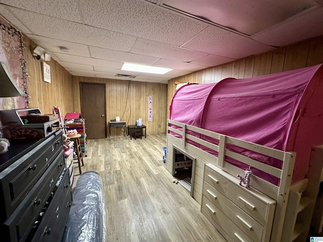 bedroom featuring light wood-style floors, a drop ceiling, wood walls, and visible vents